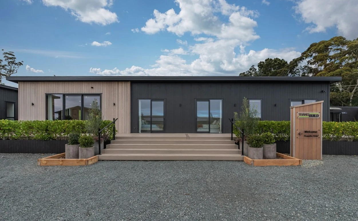 A single-storey transportable home in dark and pale vertical cladding, timber steps up to its entrance
