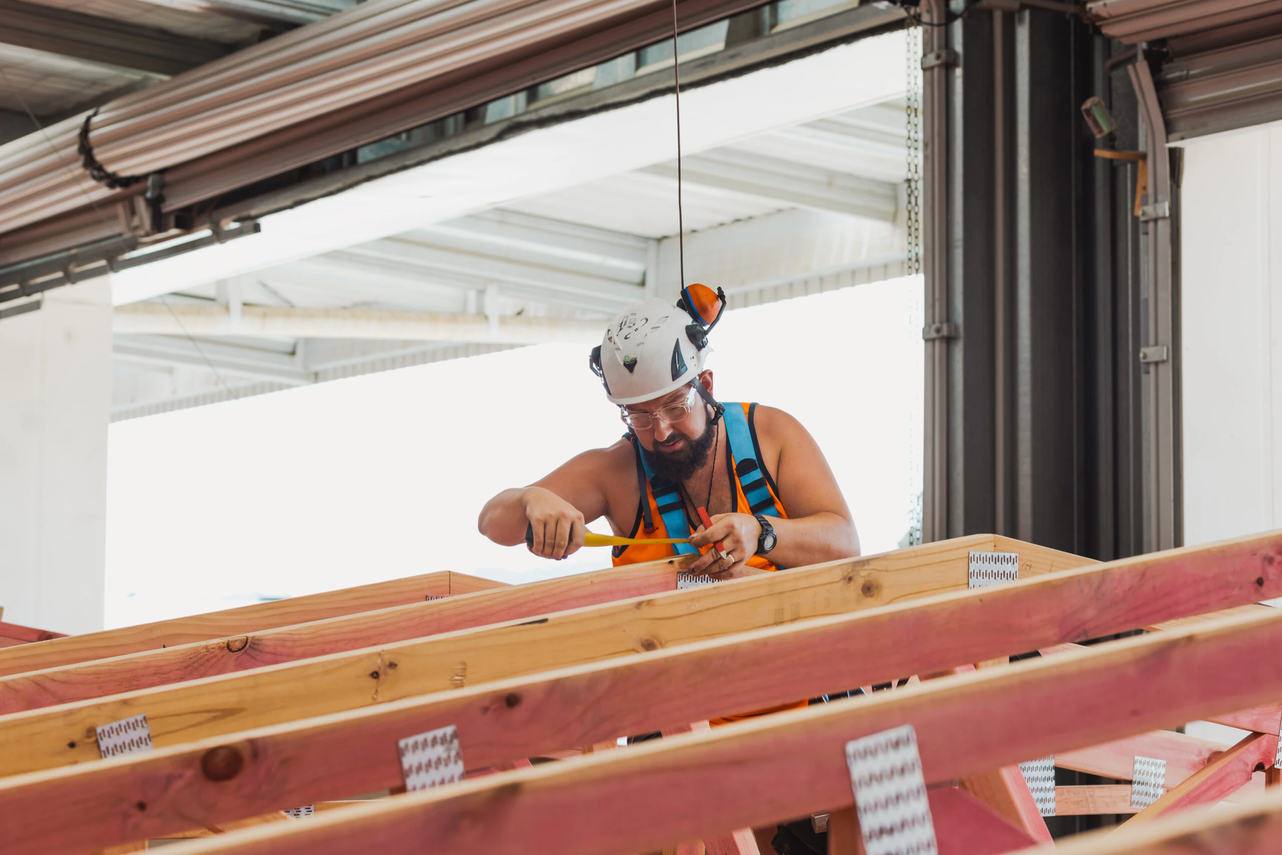 A builder measuring timber wall framing under cover during off-site manufacture